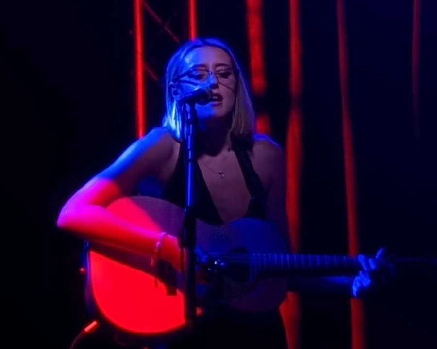 Emily Rowan sings into a microphone while playing guitar
