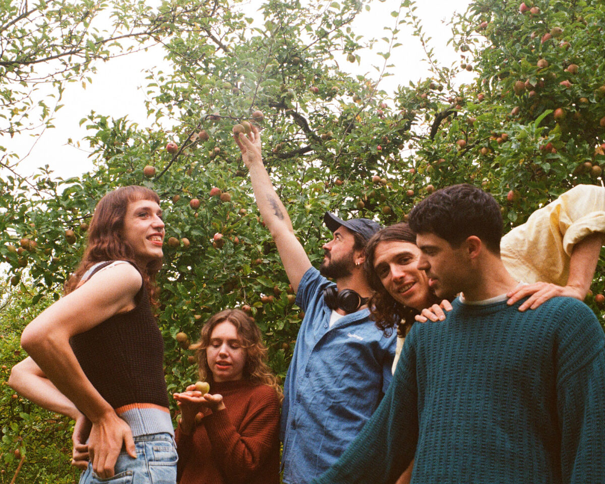 a group of five people in an apple orchard, captured with a vintage film camera aesthetic. They appear to be friends enjoying time together while apple picking.
