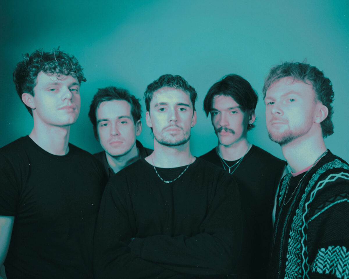 Five young men standing in a row against a teal-coloured background, appearing to be a band or music group in a promotional photo. The image has a distinctive blue-green filter or lighting that gives it a moody, atmospheric quality.